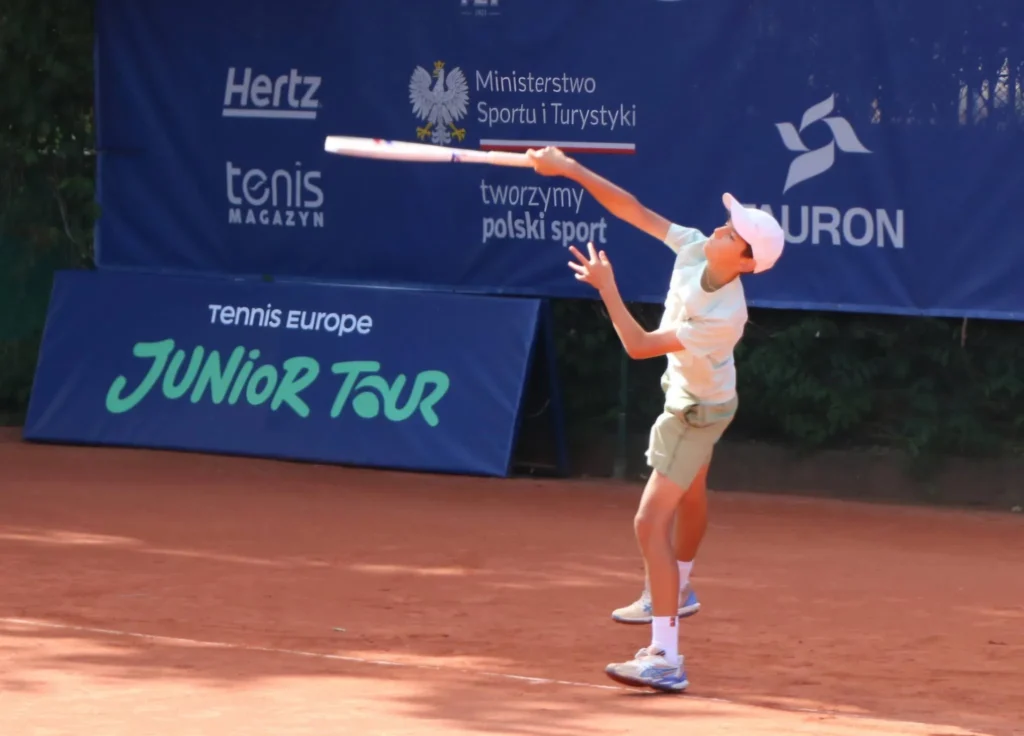 Serwis zawodnika przed banerem Tennis Europe Junior Tour